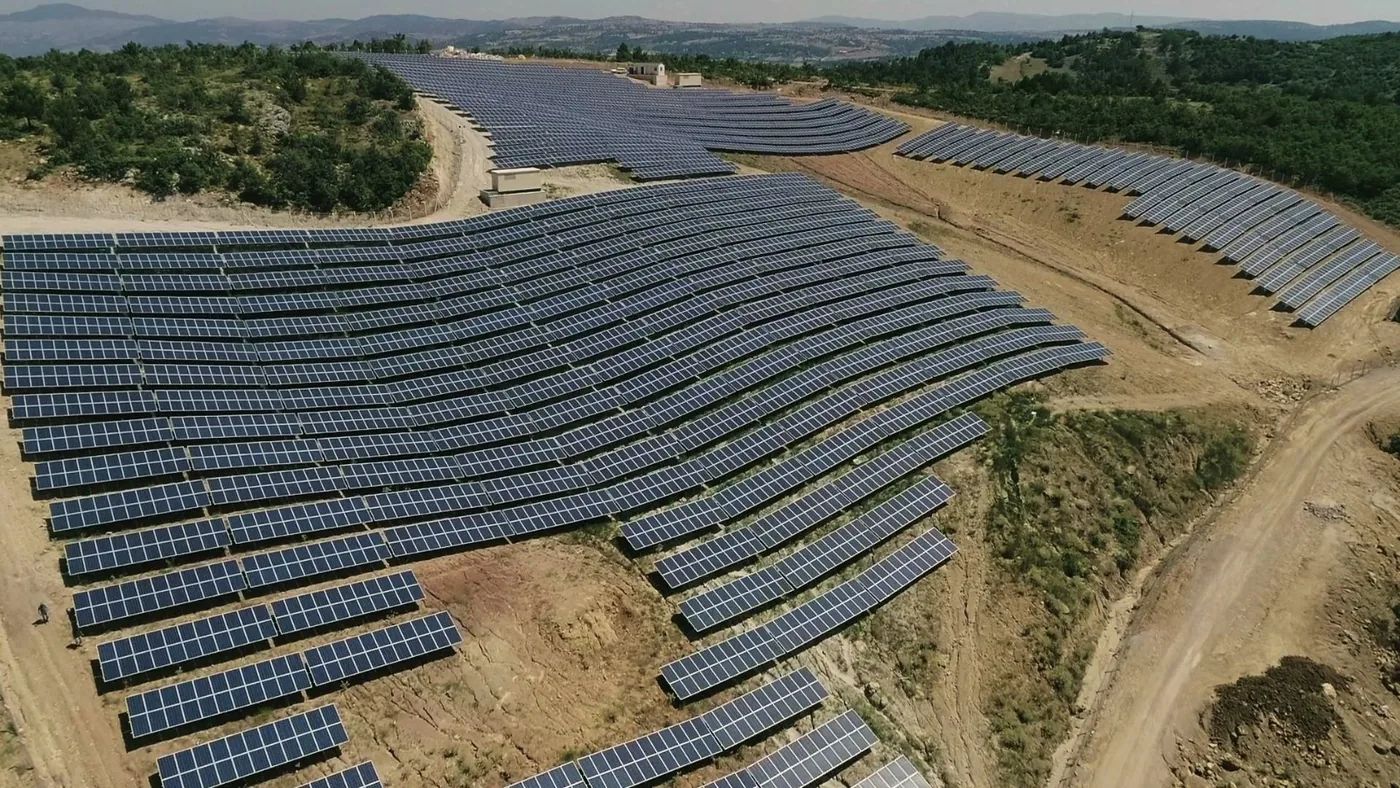 Parc fotovoltaic pe un versant, cu șiruri lungi de panouri urmărind panta terenului