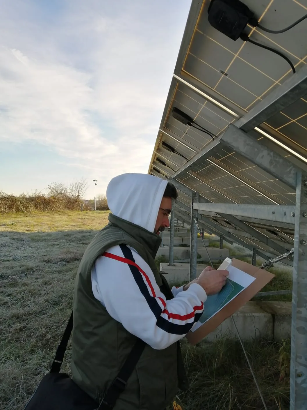 Tehnician măsurând sub o masă de panouri fotovoltaice, pe teren cu brumă