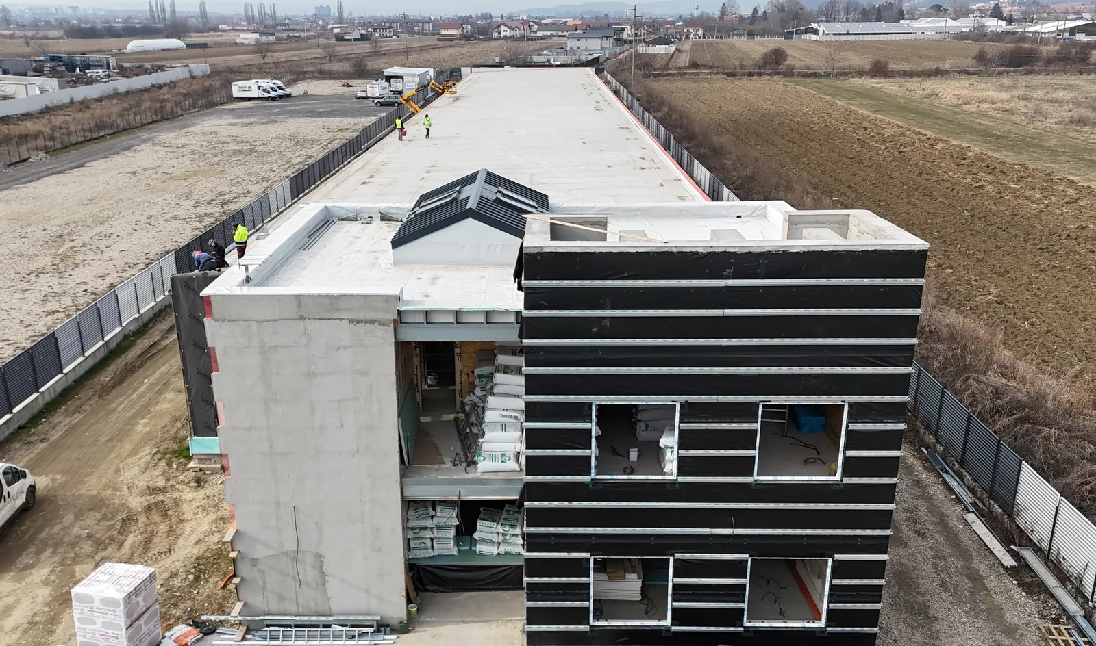 Sediul firmei în lucru, cu corpul de birouri în prim-plan și hala întinsă în spatele lui